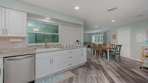 A modern kitchen with white cabinets, a built-in oven, and a dining area with wooden chairs and a table. - Pool home > 1/2 miles to beach 1 mile to Port Watch Rockets take off and land (Cape Canaveral)