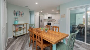 A dining area with a wooden table and chairs, a kitchen in the background, and a sliding glass door leading to an outdoor patio. - Pool home > 1/2 miles to beach 1 mile to Port Watch Rockets take off and land (Cape Canaveral)