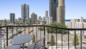 A balcony with a table and chairs overlooking a cityscape with tall buildings and a parking lot. - Surfers Paradise Beach & Ocean View Unit (Surfers Paradise)