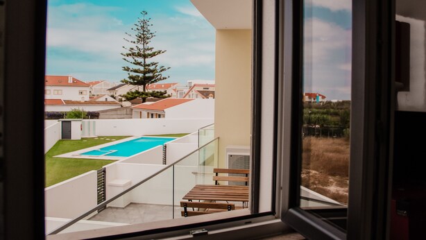 A modern balcony with a glass railing overlooking a swimming pool and a residential area. - Gold Apartment Baleal (Leiria)