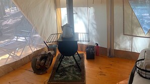 A tent interior with a central stove, a metal rack, and a chair outside. - Get in touch with nature. (Richmond)