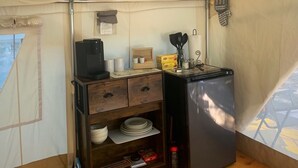 A compact kitchen area with a refrigerator, a wooden shelf with dishes, and a small table with kitchen items. - Get in touch with nature. (Richmond)