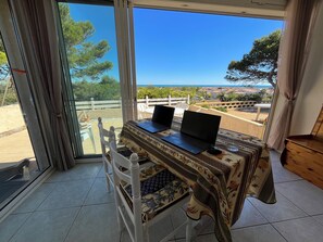Una habitación con dos portátiles sobre una mesa, una silla y vistas al mar y a la ciudad a través de amplios ventanales.