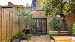 Un patio con bancos de madera, una mesita y un ventanal de vidrio que da a una habitación.