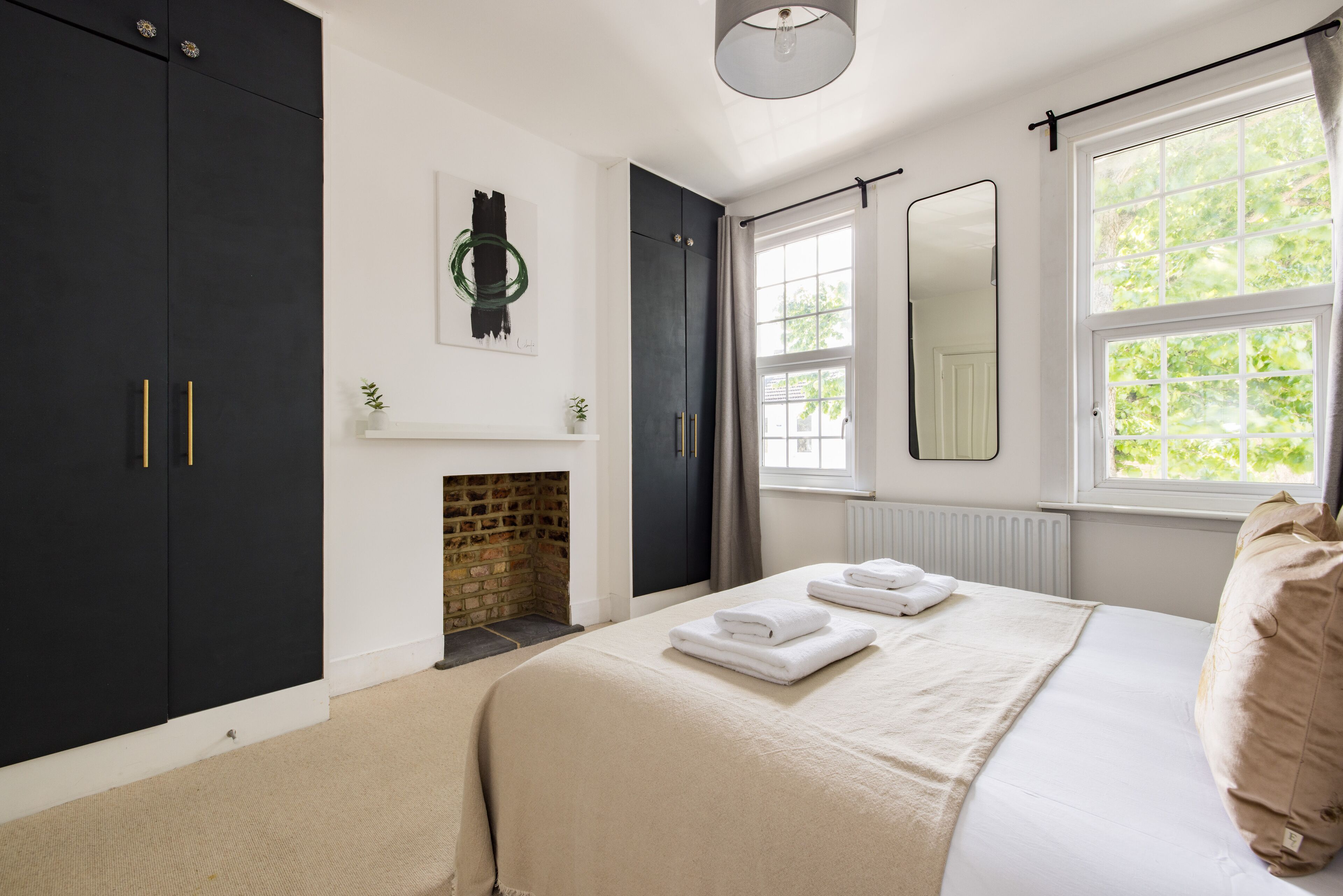 A bedroom with a bed, a fireplace, a large window, and a wardrobe.