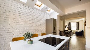 Una cocina moderna con pared de ladrillo blanco, tragaluces y una isla central con estufa integrada.