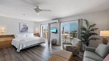 Ein Hotelzimmer mit Bett, Fernseher, einem Balkon mit Tisch und Stühlen sowie einer großen Pflanze.