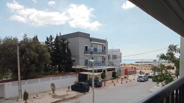 Un immeuble d’habitation doté d’un balcon, une rue pavée et des voitures garées.