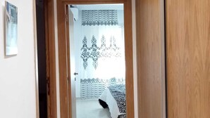 Un couloir avec une porte en bois sur la droite, un plafond blanc avec un éclairage encastré et, au fond, un rideau à motifs.