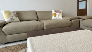 En stue med en beige hjørnesofa, et mønstret plaide og tre billeder hængt på væggen.