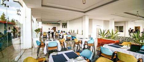 A restaurant with tables set for dining, chairs, and potted plants.