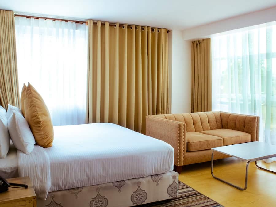 Quarto de hotel com cama, sofá, uma mesinha e telefone num criado-mudo.
