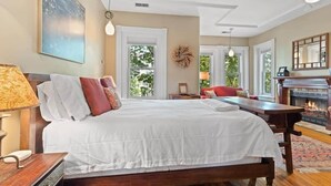 Een ruime slaapkamer met een groot bed, een open haard en uitzicht op de natuur.