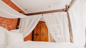 A bedroom with a canopy bed, wooden wardrobe, and a red patterned wall.
