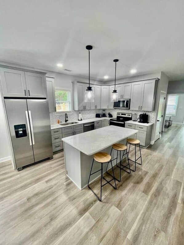 A modern kitchen with a central island, bar stools, stainless steel appliances, and pendant lighting.