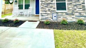 A two-story house with a stone facade, a blue door, and a covered porch with chairs.