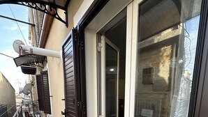 Un balcon étroit doté d’une porte-fenêtre coulissante, d’une rambarde en métal et d’un petit espace extérieur aménagé pour s’asseoir.