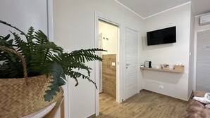 Une chambre à coucher moderne avec un plancher en bois, un téléviseur fixé au mur, une table de chevet avec une lampe et une grande plante en pot.