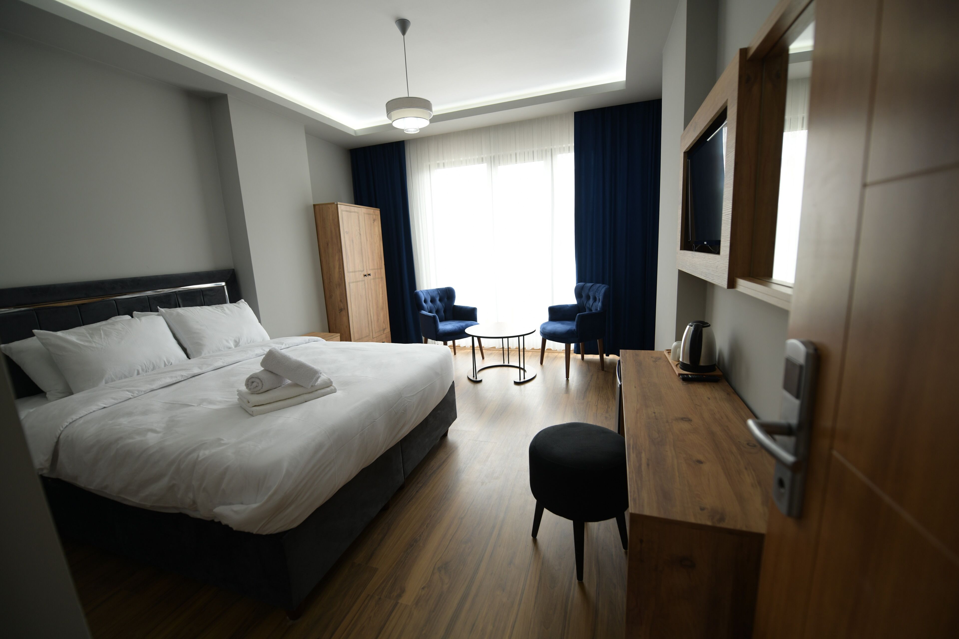 A hotel room with a bed, a desk, two chairs, a TV, and a wardrobe.
