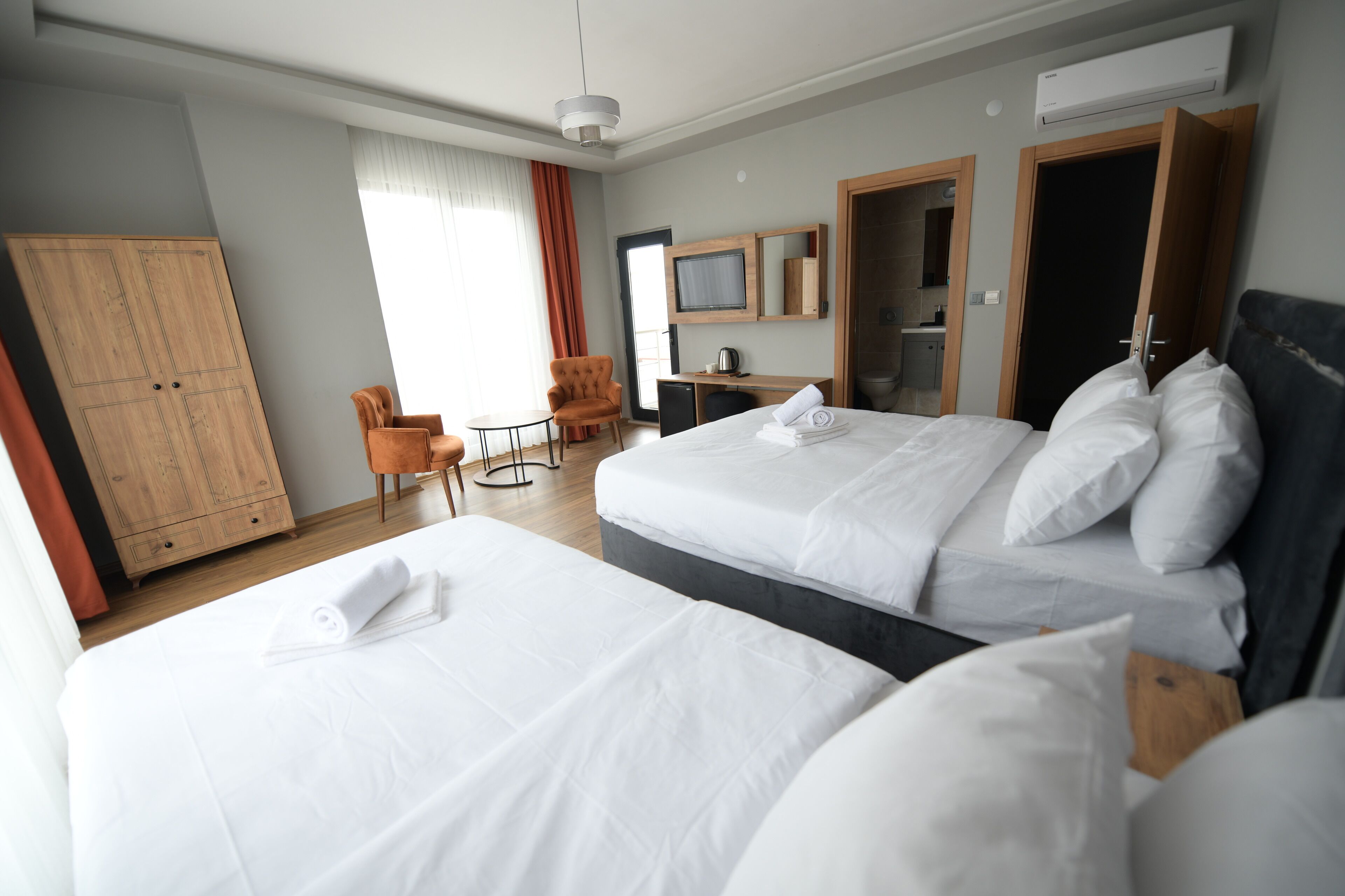 A hotel room with two beds, a desk, a chair, a television, and an air conditioning unit.