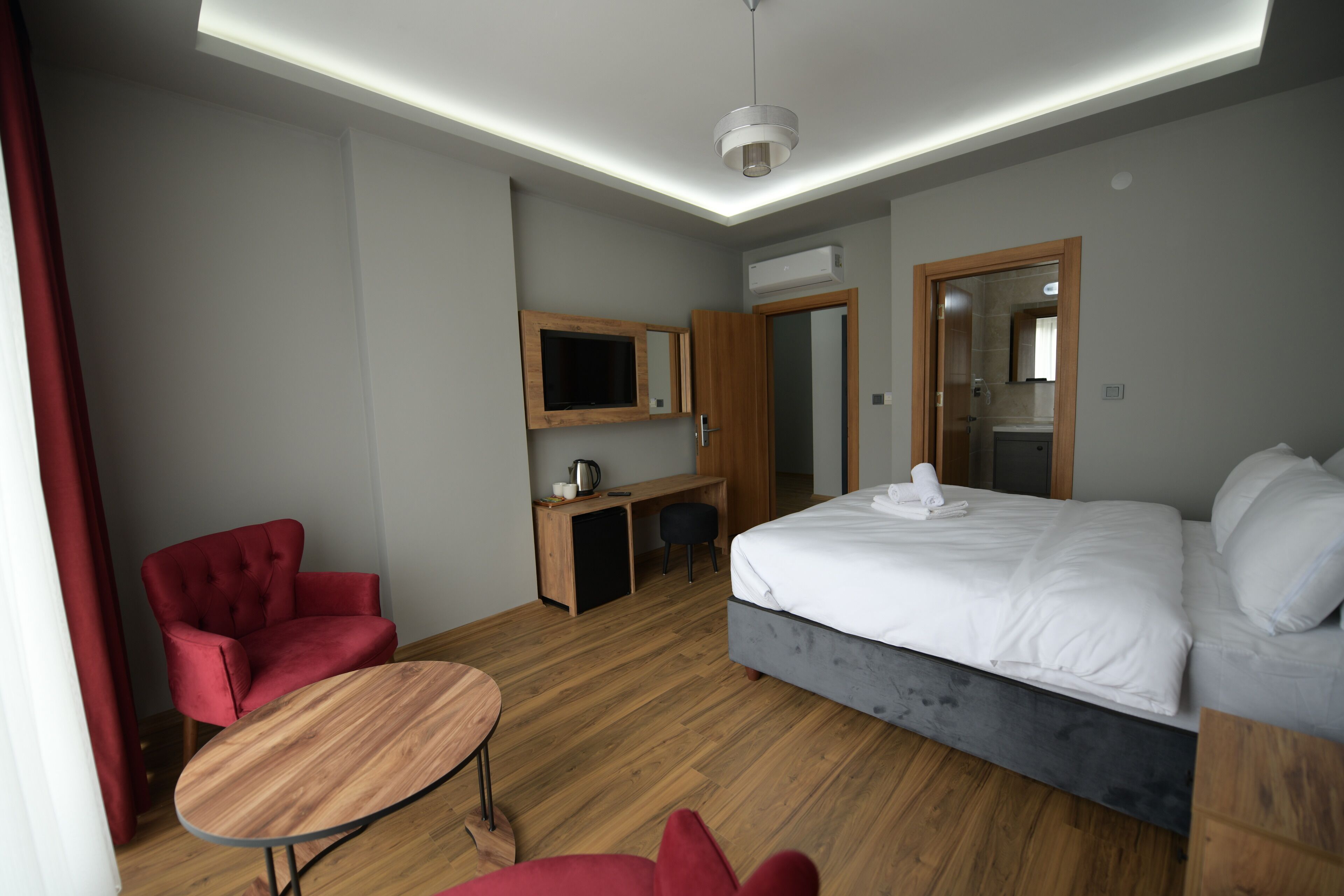 A modern hotel room with a large bed, a desk, a red chair, and a small table.