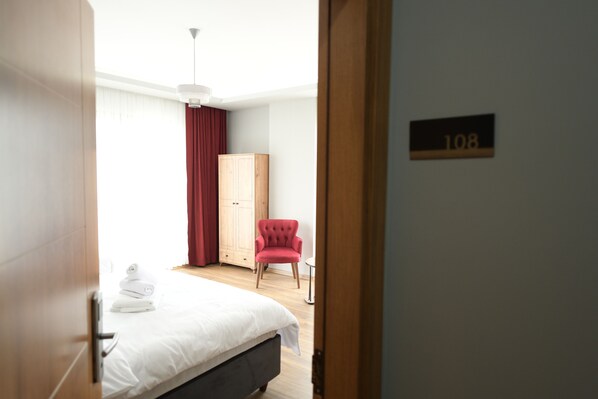 A hotel room with a bed, a red chair, a wooden wardrobe, and a number sign on the wall. - Poal Group Hotel (Trabzon)
