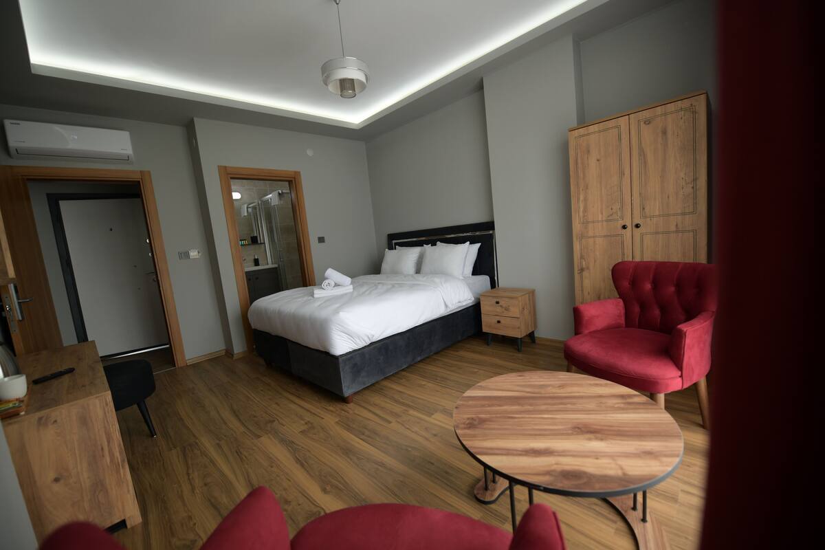 Ein modernes Hotelzimmer mit einem Bett, einem Holzschrank, einem roten Sessel, einem kleinen Holztisch und einem Spiegel.
