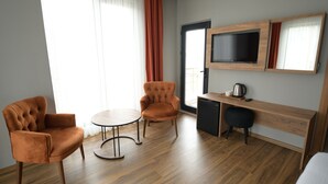 Une chambre d’hôtel moderne avec un plancher en bois, deux fauteuils, une petite table ronde, un bureau avec une télévision et une machine à café.