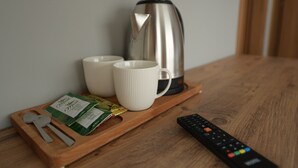 Un plateau en bois sur lequel se trouvent deux tasses blanches, une bouilloire en acier inoxydable, une télécommande et quelques paquets de collations, le tout posé sur une table en bois.