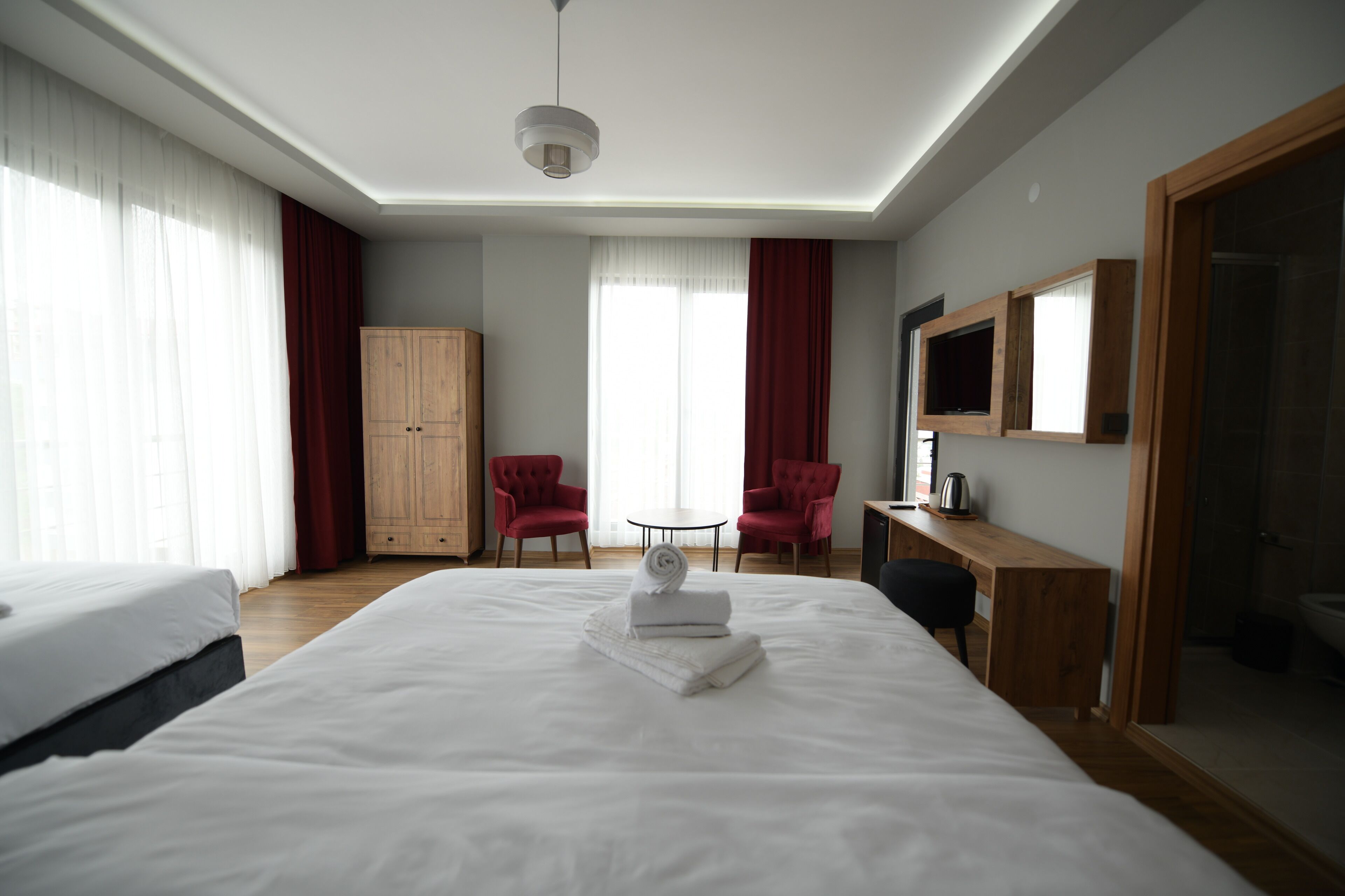 A hotel room with a large bed, a wooden wardrobe, two red armchairs, a small round table, and a TV mounted on the wall.