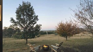 An outdoor seating area with a fire pit and chairs, surrounded by trees and a grassy field. - The High Country Views Escape by Tiny Away (Table Top)