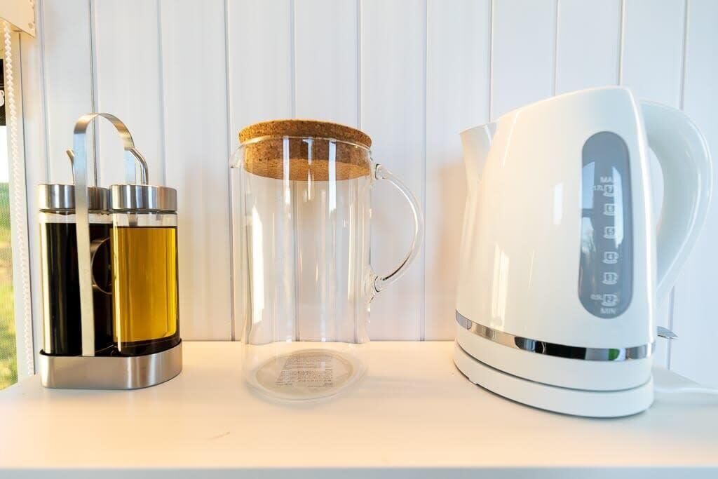 Un plan de travail de cuisine avec une bouilloire en acier inoxydable, un récipient en verre doté d’un couvercle en liège et un récipient en métal muni d’une anse.