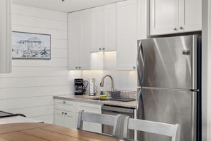 Una cocina moderna con gabinetes blancos, electrodomésticos de acero inoxidable, una cafetera y un lavamanos.