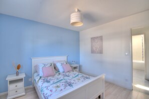A bedroom with a bed, nightstands, a wall art piece, and a door leading to another room.