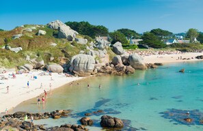 Une plage avec une eau claire, de gros rochers et des gens qui prennent un bain de soleil.