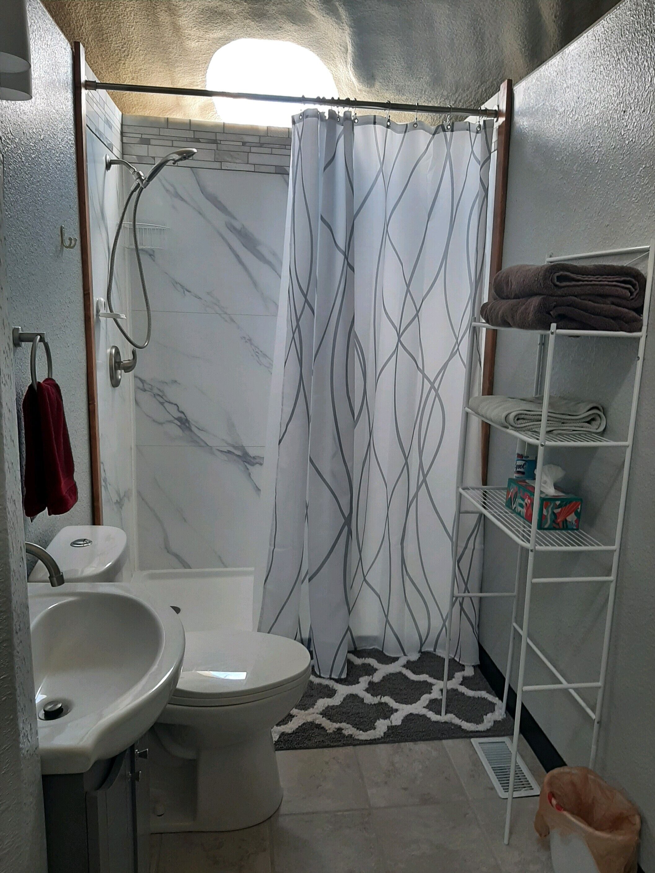 A bathroom with a shower, toilet, sink, and towel rack.