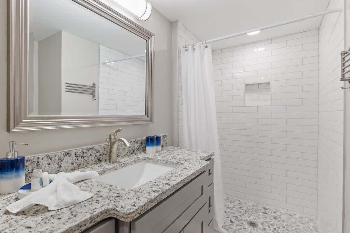A bathroom with a granite countertop sink, a large mirror, a shower with white tiles, and a towel on the counter.