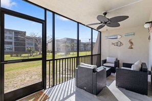 A balcony with wicker furniture, a ceiling fan, and a view of buildings and greenery. - Loggerhead 261- Gorgeous Two Bedroom Condo with Fantastic Amenities (Sanibel)