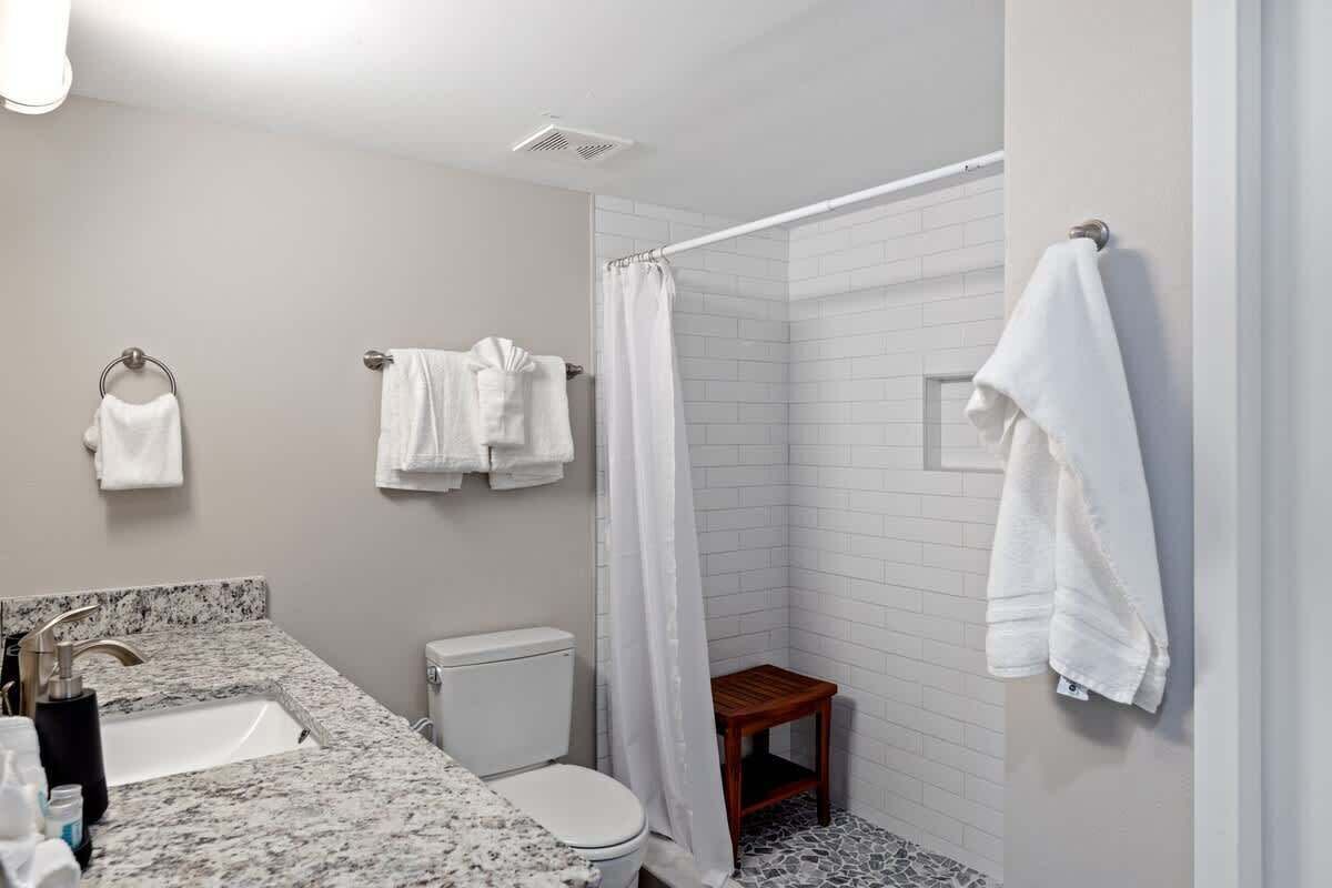 Een badkamer met een wastafel, toilet, douche en een klein houten krukje.