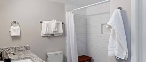 Een badkamer met een wastafel, toilet, douche en een klein houten krukje.