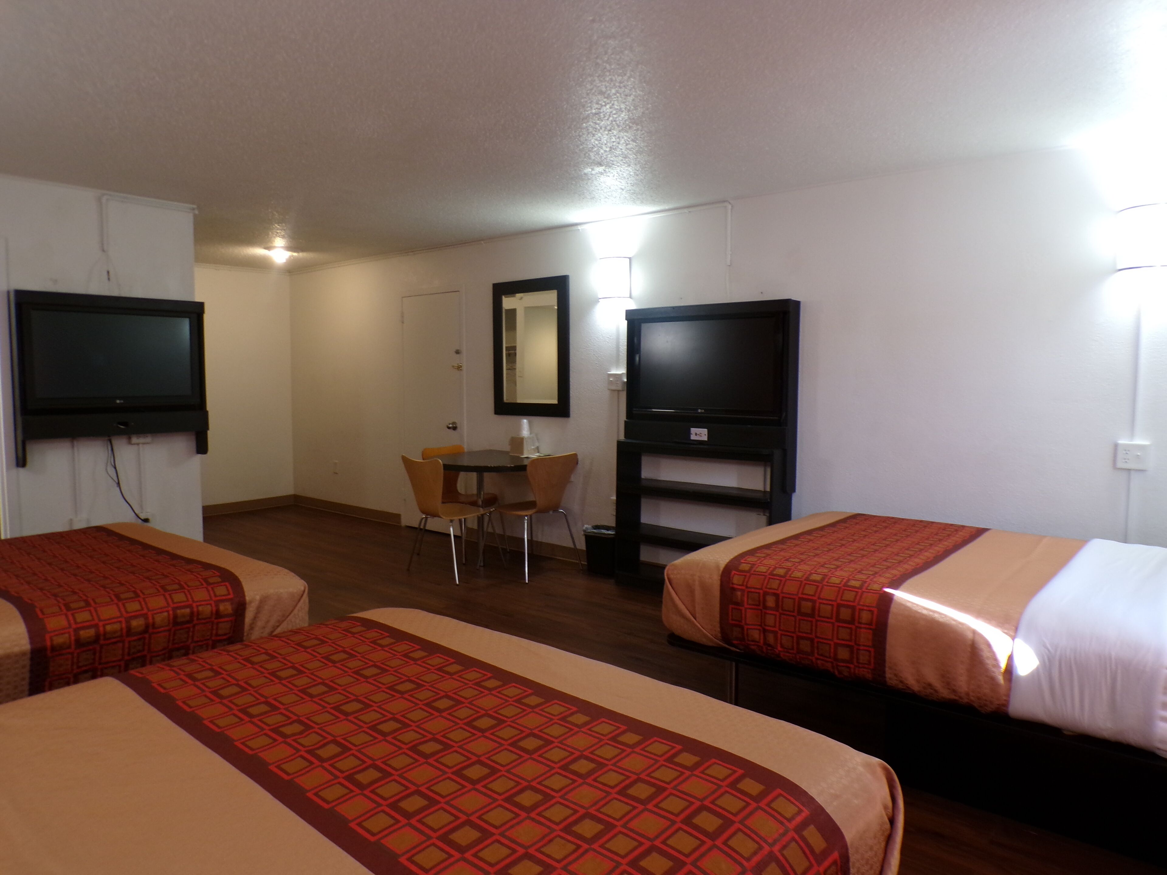 A hotel room with two beds, a desk, a chair, and two televisions.