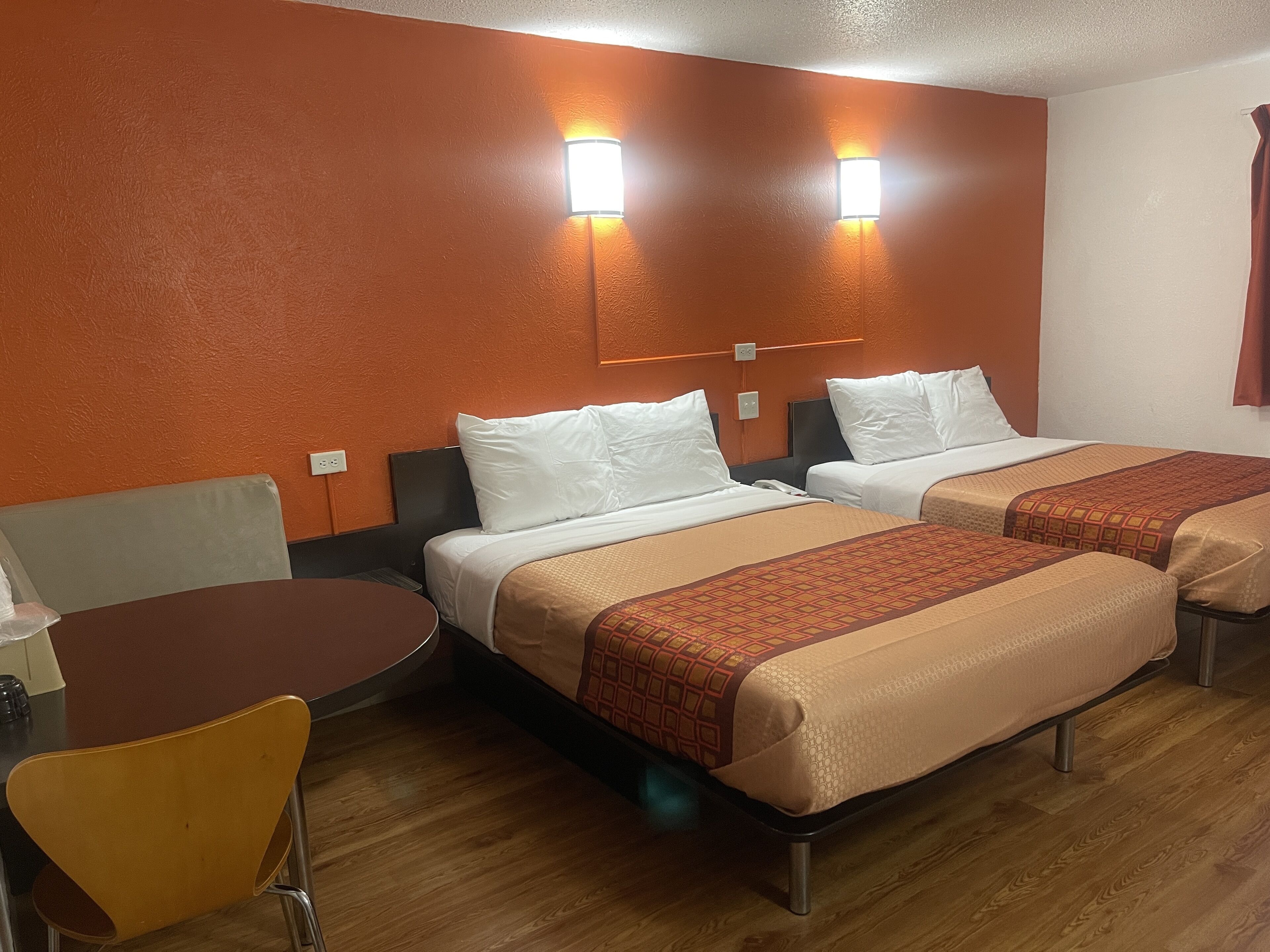 A hotel room with two beds, a small table, and a chair.