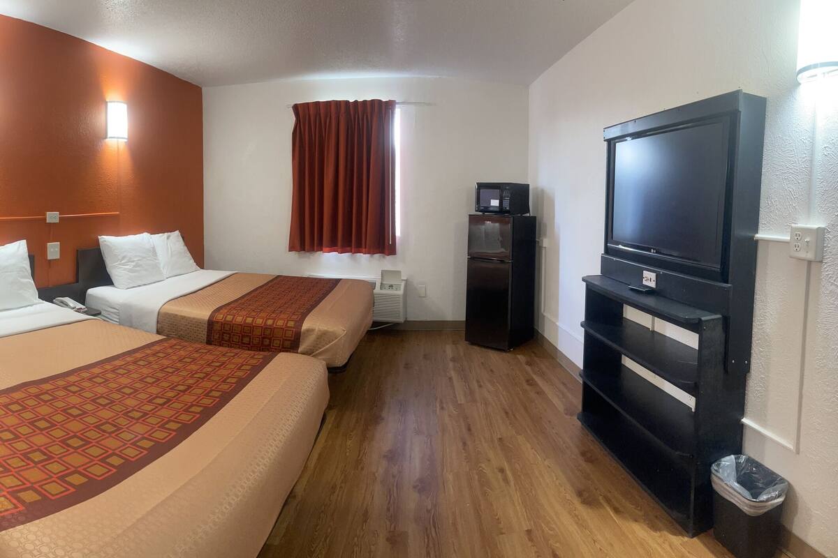 A hotel room with two beds, a desk, a chair, a TV, and a microwave.