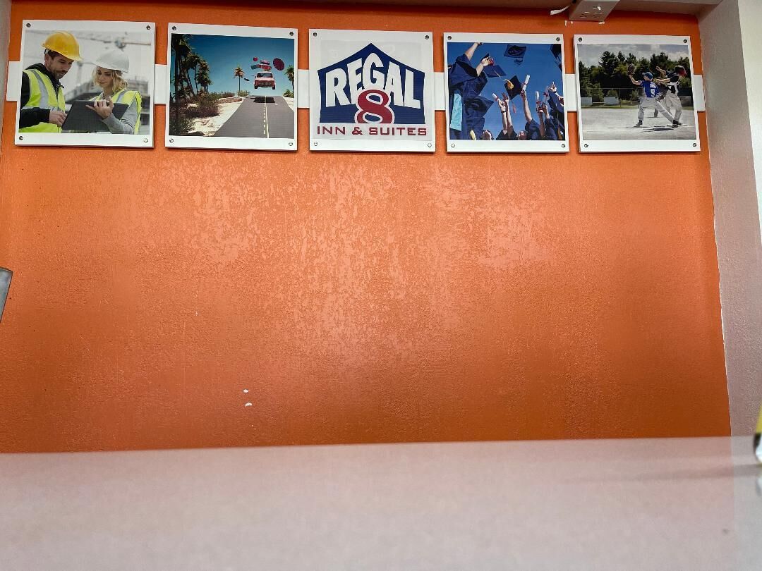 A wall with four framed photos depicting various scenes: construction workers, a road with a vehicle, a logo for Regal Inn & Suites, and a graduation ceremony.