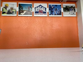 A wall with four framed photos depicting various scenes: construction workers, a road with a vehicle, a logo for Regal Inn & Suites, and a graduation ceremony.