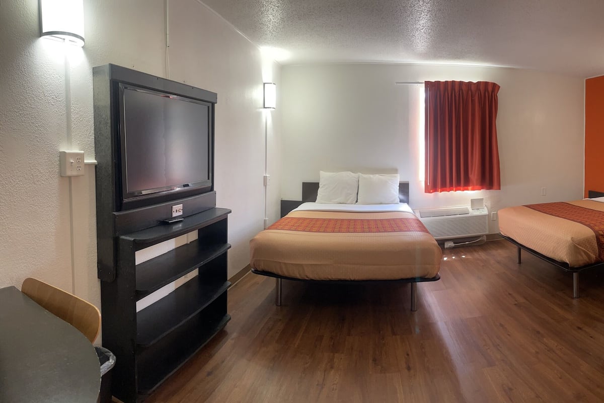 A hotel room with three beds, a TV, and a desk.