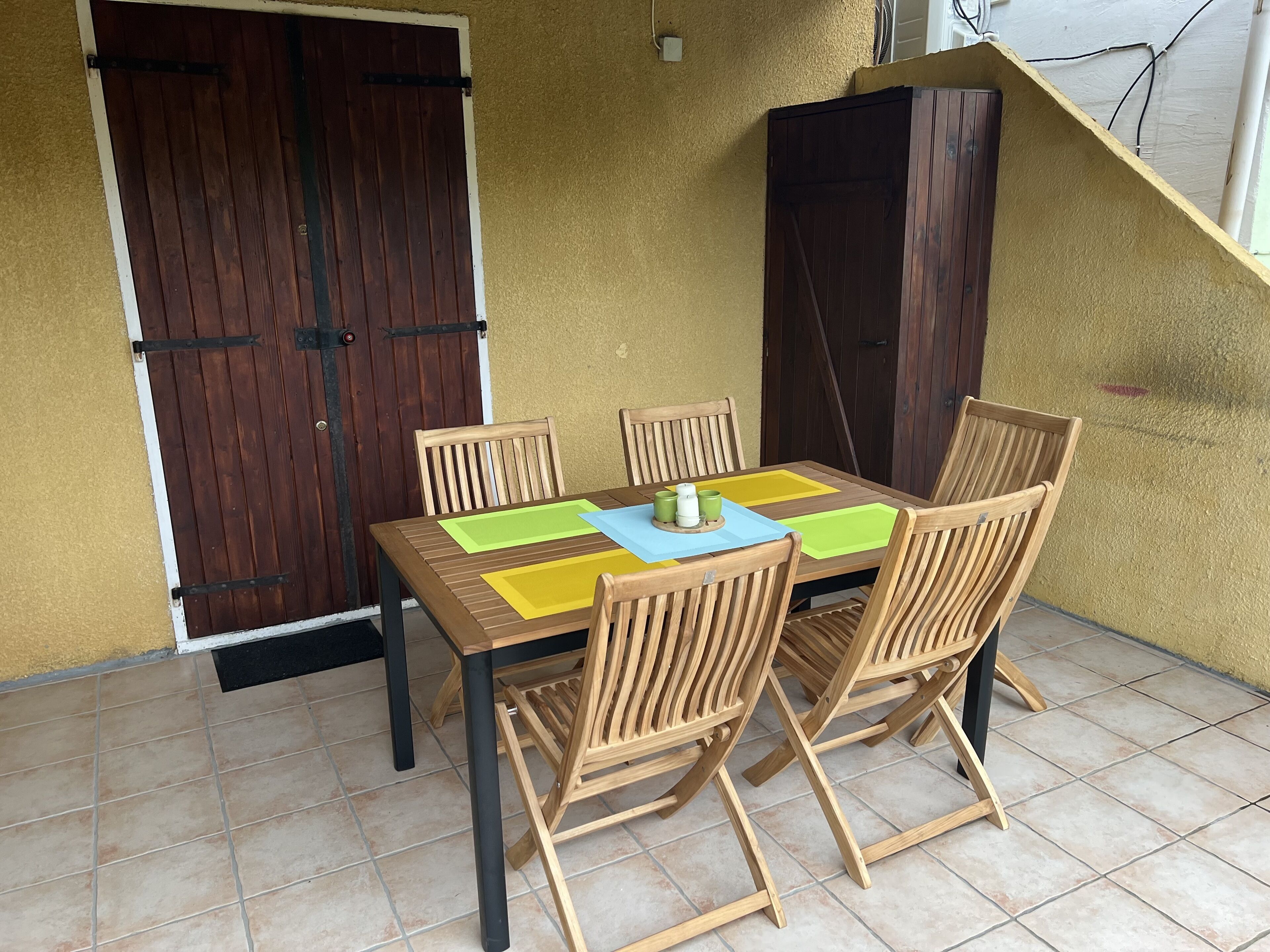 Une table en bois avec quatre chaises, un sol carrelé et un mur jaune orné de deux portes en bois.
