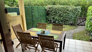 Une terrasse avec une table et des chaises en bois, entourée d’une haie verdoyante et d’une clôture en bois.