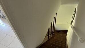 Un escalier en bois avec une rampe, des murs blancs et un sol carrelé.