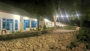 A building with multiple rooms, each with blue-framed windows and doors, a stone pathway leading to the entrance, and outdoor seating. - THE VILLAGE INN Rua Beach  (Wanokaka)
